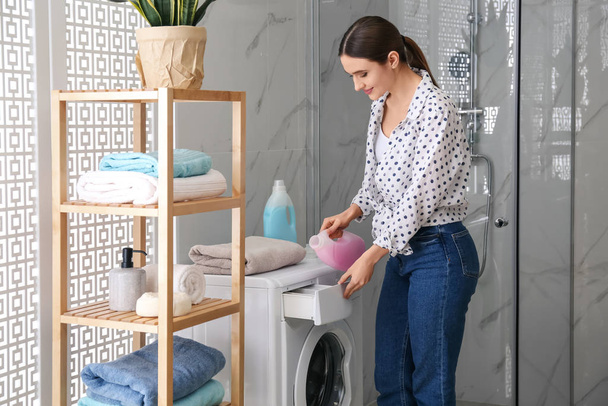 Woman pouring detergent into washing machine drawer in bathroom. - Foto, Imagen