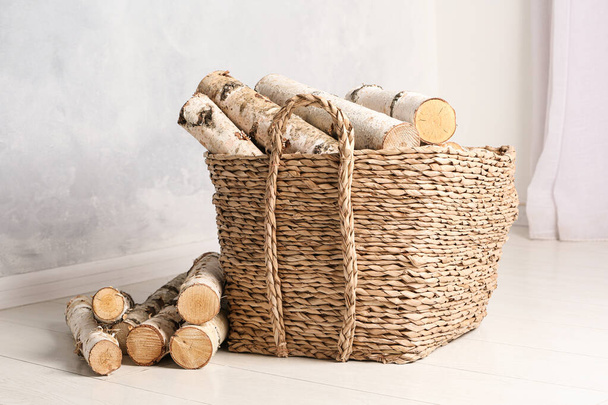 Wicker basket with cut firewood on white floor indoors - Фото, изображение