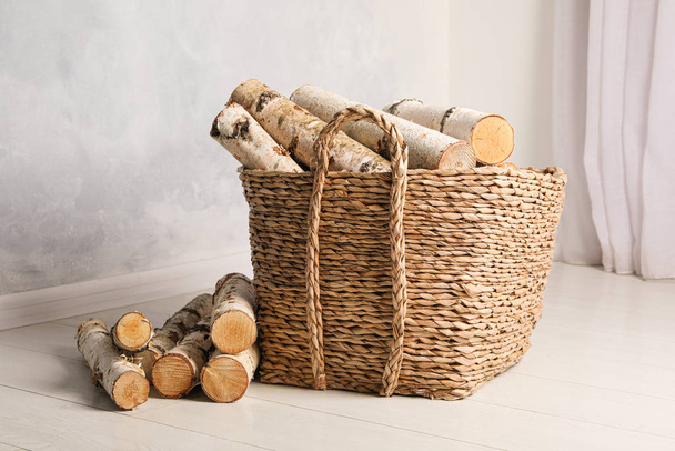 Wicker basket with cut firewood on white floor indoors - Foto, imagen