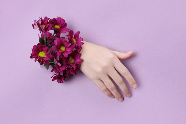 Beauty Hand with flowers in a hole in a purple paper background. - Foto, Bild