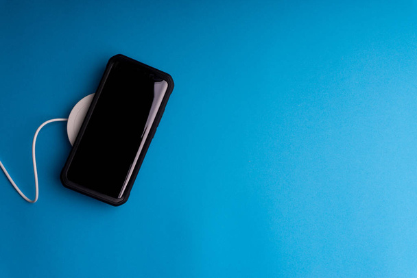 Smartphone charging on a charging pad or dock on blue background.Wireless charging and copy space  - Fotografie, Obrázek
