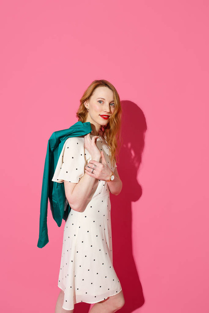 Beautiful fashionable young blonde woman posing in a studio, wide opened green jacket and summer dress. Long wavy hairstyle. Bright pink background. Fashion autumn spring summer photo - Φωτογραφία, εικόνα