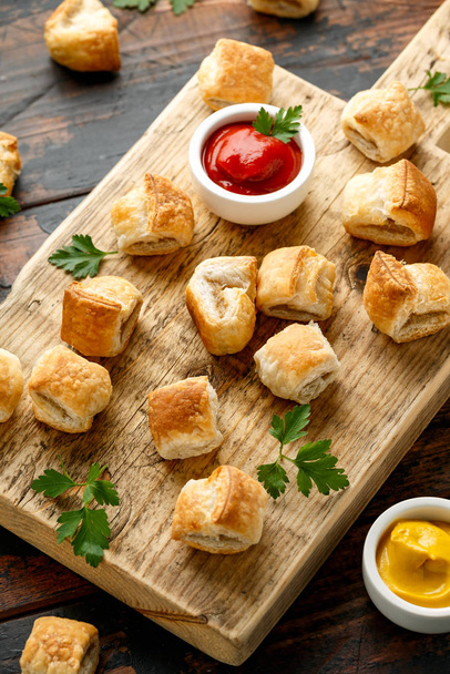 Pork sausage rolls with mustard and ketchup sauce on wooden board - 写真・画像