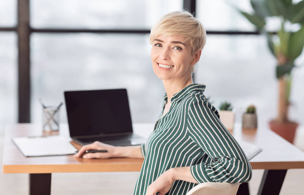 Επιχειρηματίας που κάθεται στο Laptop χαμογελώντας στην κάμερα ποζάροντας στο χώρο εργασίας - Φωτογραφία, εικόνα