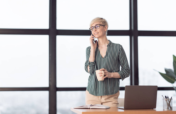 Señora de los negocios hablando en el teléfono móvil de pie en el lugar de trabajo
 - Foto, imagen