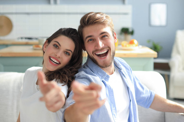 Portrait of cute young couple pointing and laughing, sitting in sofa. - Φωτογραφία, εικόνα
