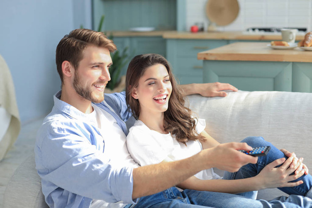 Young loving couple on sofa at home watching tv and laughing. - Photo, image
