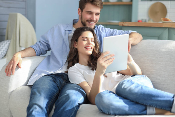 Young couple watching media content online in a tablet sitting on a sofa in the living room. - Foto, Imagem