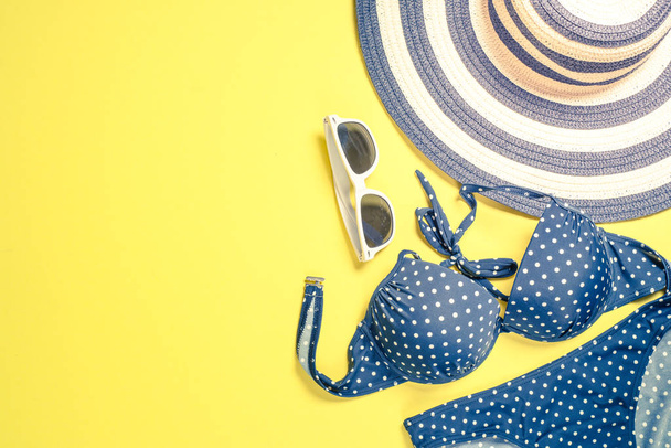 Концепція літніх подорожей. Смугастий капелюх, купальник і сонцезахисні окуляри на жовтому
. - Фото, зображення