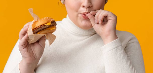 Nicht wiederzuerkennen Fat Girl Holding Burger Und Licking Fingers Mit Vergnügen - Foto, Bild