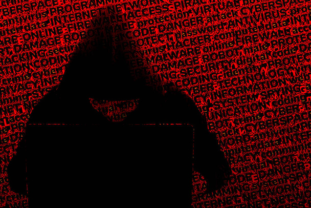 The silhouette of a hacker in a hood behind a laptop, against a  - Photo, Image