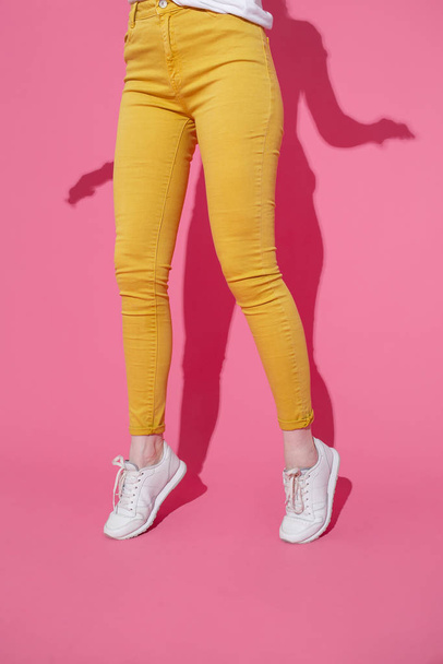 Female feet in trendy yellow jeans and white sneakers on a pink background - Φωτογραφία, εικόνα