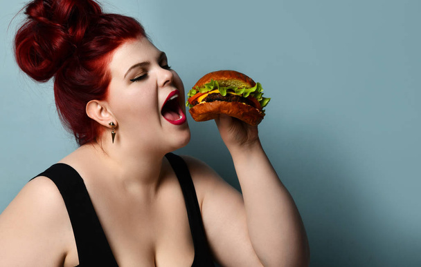 Happy size-plus overweight fat woman happy hold burger cheeseburger barbeque sandwich with beef  on pastel turquoise - Photo, image