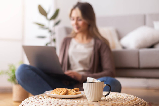 Femme naviguant sur ordinateur portable à la maison, se concentrer sur la tasse de café
 - Photo, image
