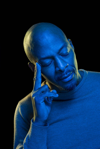 Kolorowy portret mężczyzny z przemyślanym wyrazem twarzy i zamkniętymi oczami. Światło z niebieskim filtrem żelu  - Zdjęcie, obraz