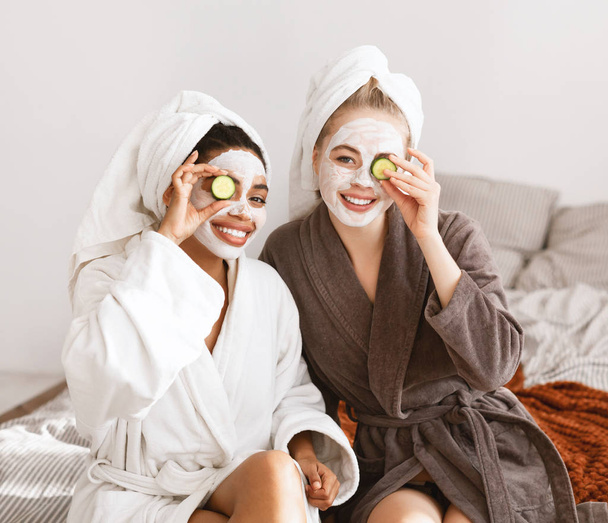 Happy spa girlfriends with face masks covering eyes with cucumber - Photo, Image