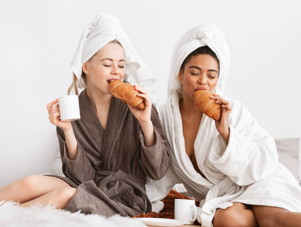 Multiethnic spa girlfriends enjoying breakfast, sitting on bed - Foto, Imagem