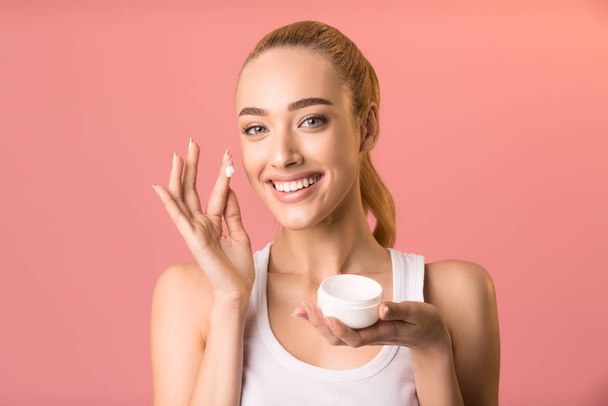 Girl Applying Facial Cream Holding Jar Standing On Pink Background - Foto, afbeelding