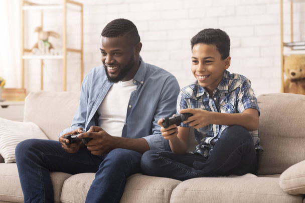 Ενθουσιασμένος μαύρο αγόρι που παίζει βιντεοπαιχνίδια με τον μπαμπά στο σπίτι - Φωτογραφία, εικόνα