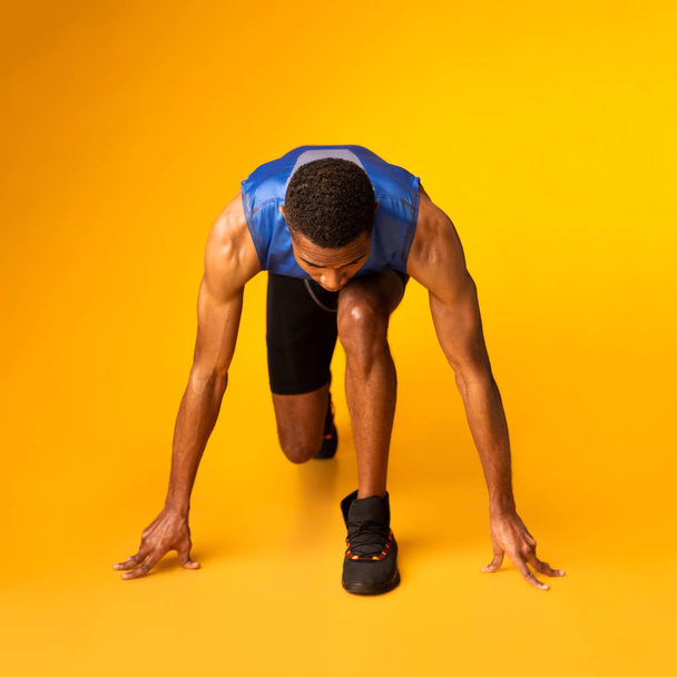 Serieuze afro guy bereidt zich voor op een run in oranje studio - Foto, afbeelding
