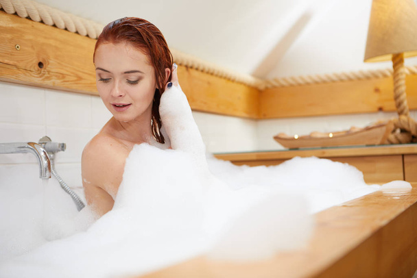 Portrait of redhaired woman playing with foam in bathtub - Фото, зображення