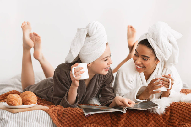 Mujeres sonrientes en batas de baño y toallas acostadas en la cama
 - Foto, Imagen