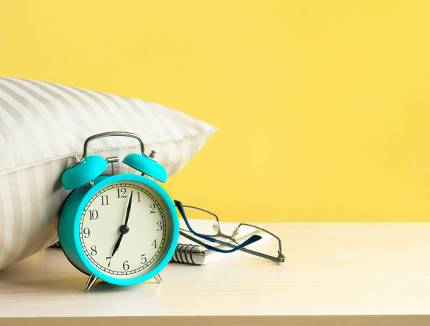 Morgens türkis Wecker neben dem Kissen auf dem Nachttisch auf gelbem Wandhintergrund - Foto, Bild