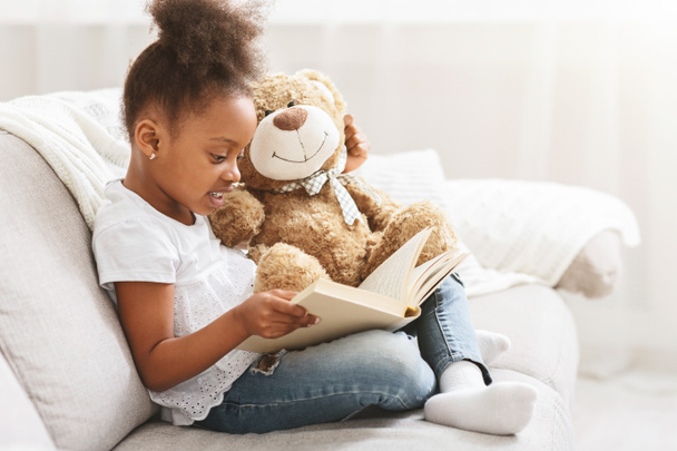 Μικρό κορίτσι Αφρο κρατώντας αρκουδάκι και διαβάζοντας το βιβλίο - Φωτογραφία, εικόνα