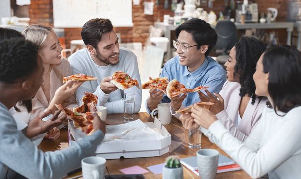 Дружелюбная международная команда наслаждается пиццей вместе в офисе
 - Фото, изображение