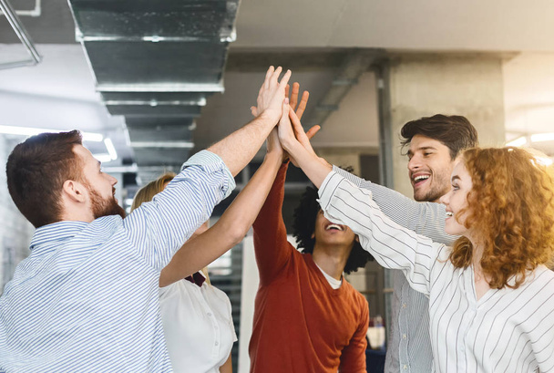 Multiethnic millennial friends giving high five in office - 写真・画像