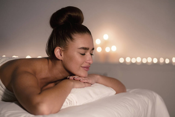 Koncepcja masażu. Zrelaksowana kobieta w spa, leżąca na stole do masażu - Zdjęcie, obraz