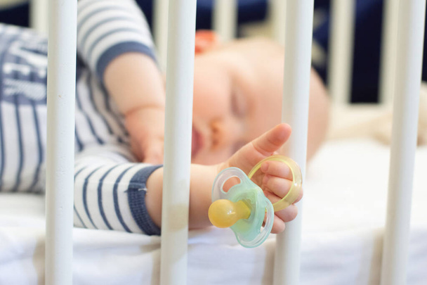 Blaues Bild eines kleinen Jungen, der friedlich schläft und eine Schnullerattrappe in der Hand hält. Selektiver Fokus auf eine Attrappe - Foto, Bild