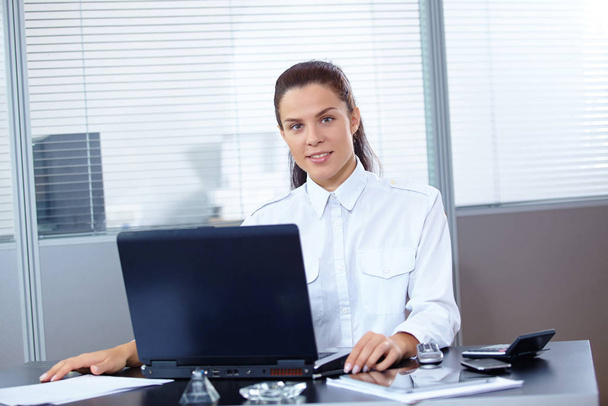 Young beautiful businesswoman sitting with laptop at workplace - Фото, изображение