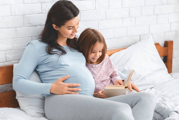 Pregnant lady reading fairy tales to her little cute daughter - Foto, Bild