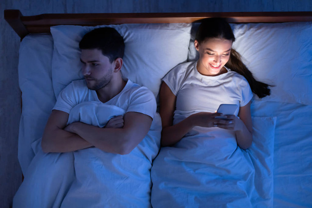 Infiel novia mensajes de texto acostado cerca de novio en la cama, Vista superior
 - Foto, imagen