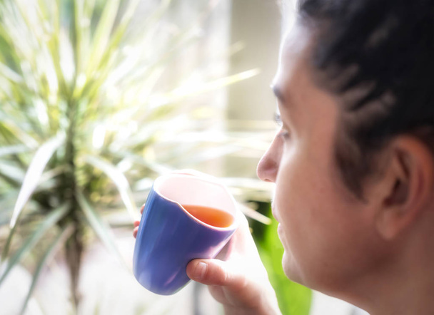Latino nainen kotona ikkunan edessä rentouttava olohuoneessaan juo teetä, valikoiva terävyys, keskittyä kuppi, vintage värit
 - Valokuva, kuva