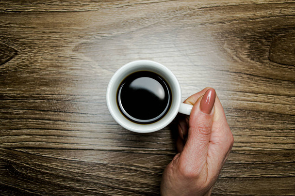 Taza de café en una mano femenina sobre un fondo de parquet
 - Foto, Imagen