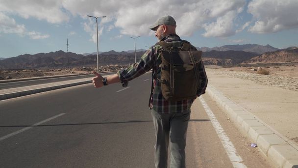 シニア男性は道路を歩くとヒッチハイクの看板に親指を表示 - 写真・画像