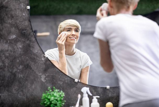 Hölgy alkalmazása Skincare termék használata pamut párna álló fürdőszobában - Fotó, kép