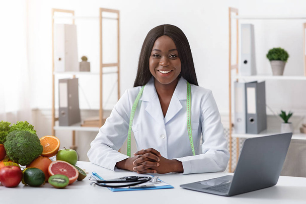 Mosolygó orvos táplálkozási orvos zöldséggel és gyümölccsel az irodában - Fotó, kép
