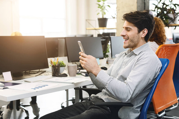 Excited guy looking at mobile phone screen, office interior - Fotoğraf, Görsel