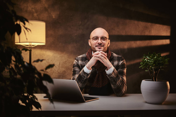 Bald european well-dressed smiling businessman sitting in the office at a table with notebook, wearing stylish jacket and a scarf - Foto, Bild