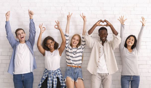 Živí mladí přátelé zvedají ruce a ukazují různorodá gesta - Fotografie, Obrázek