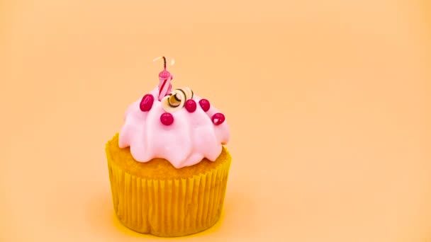 verjaardag cupcake met een rood aangestoken kaars, op oranje achtergrond. - Video