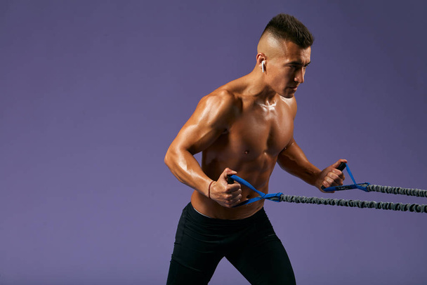 deportista sexy haciendo ejercicios con expansor aislado sobre fondo azul
 - Foto, imagen
