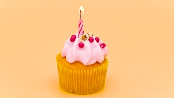 birthday cupcake with a red lit candle, on orange background. - Video