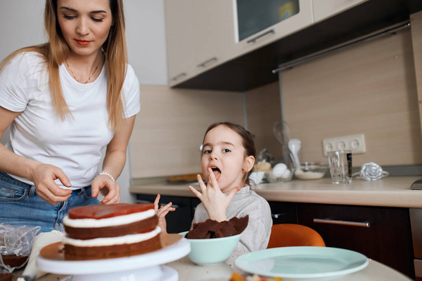 little beautiful girl licking her fingers after cooking cake with mommy - Foto, imagen