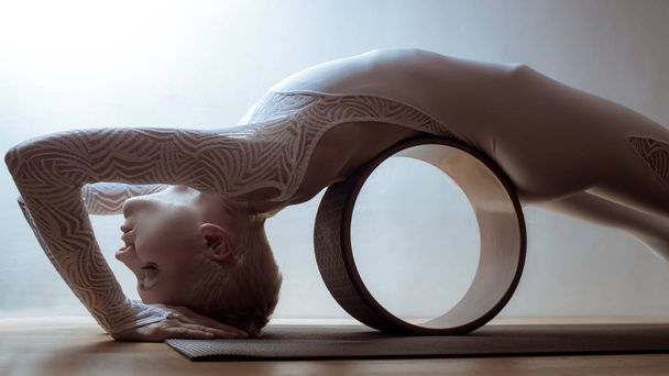 Beautiful young woman yogi with yoga wheel on light background - Fotoğraf, Görsel
