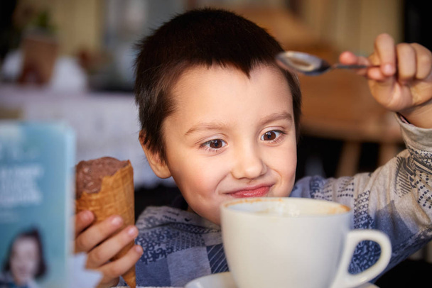 Glücklicher Junge hält Eistüte in der Hand und spielt mit Teelöffel - Foto, Bild
