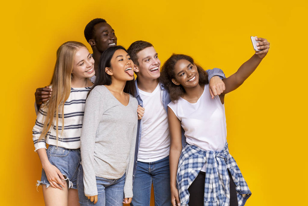 Fröhliche Gruppe multiethnischer Freunde macht Selfie vor gelbem Hintergrund - Foto, Bild